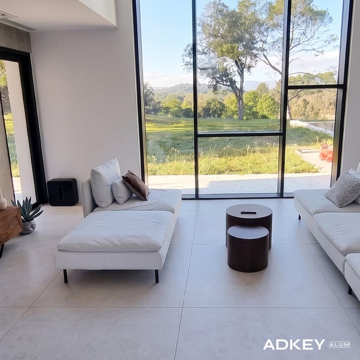 Salon contemporain encadré par un mur-rideau en aluminium noir mat ouvrant sur un jardin — projet AdKey Aluminium à Boubana
